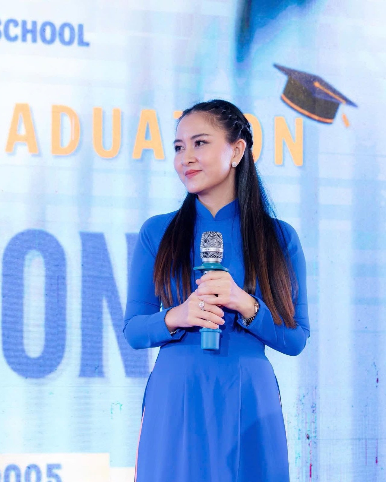 Trần Thùy Trang trong tà áo dài xanh, phát biểu tại một lễ tốt nghiệp của trường